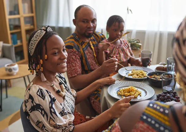 Une famille partage un repas autour d'une table en portant des vêtements aux motifs africains.
