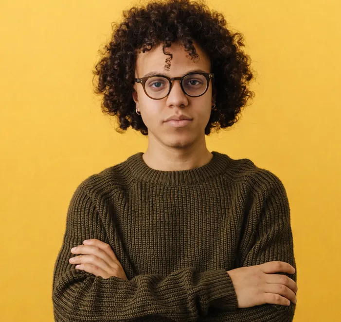 Un garçon à lunettes et aux cheveux frisés croise les bras.