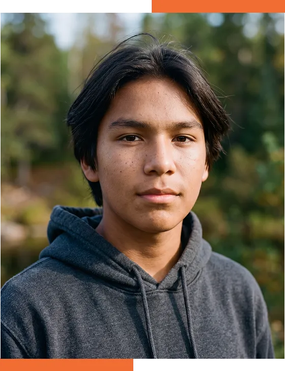 Un adolescent au regard calme pose à l’extérieur devant un arrière-plan flou d’arbres et de verdure.