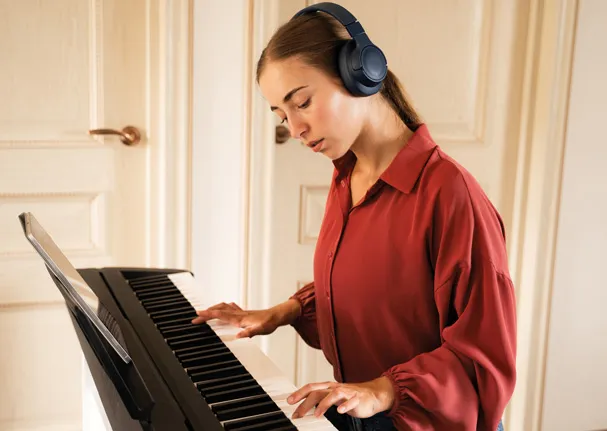 Une adolescente portant un casque d’écoute est concentrée sur son jeu au piano électrique.